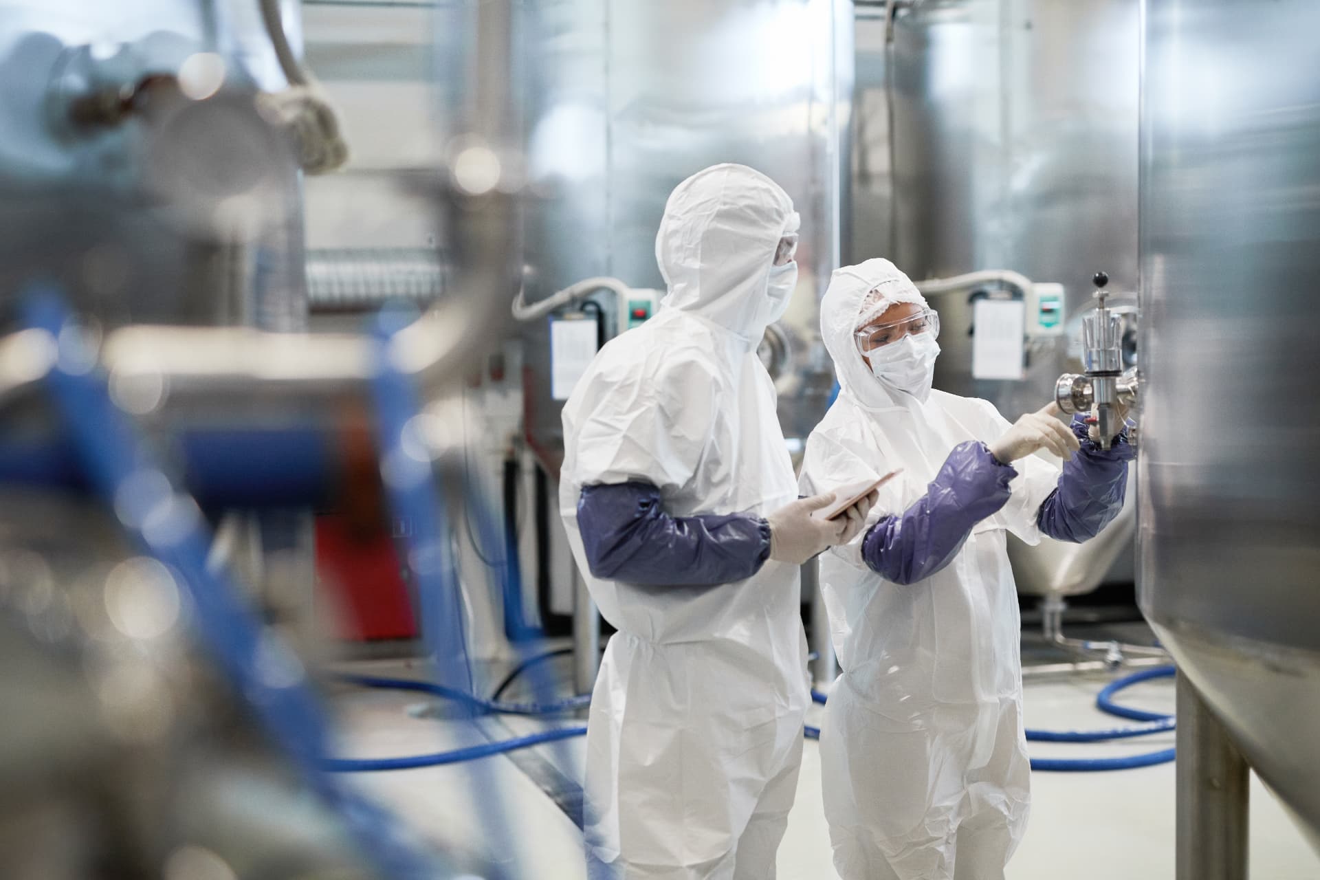 Technicians in clean suits inspecting equipment at an industrial plant