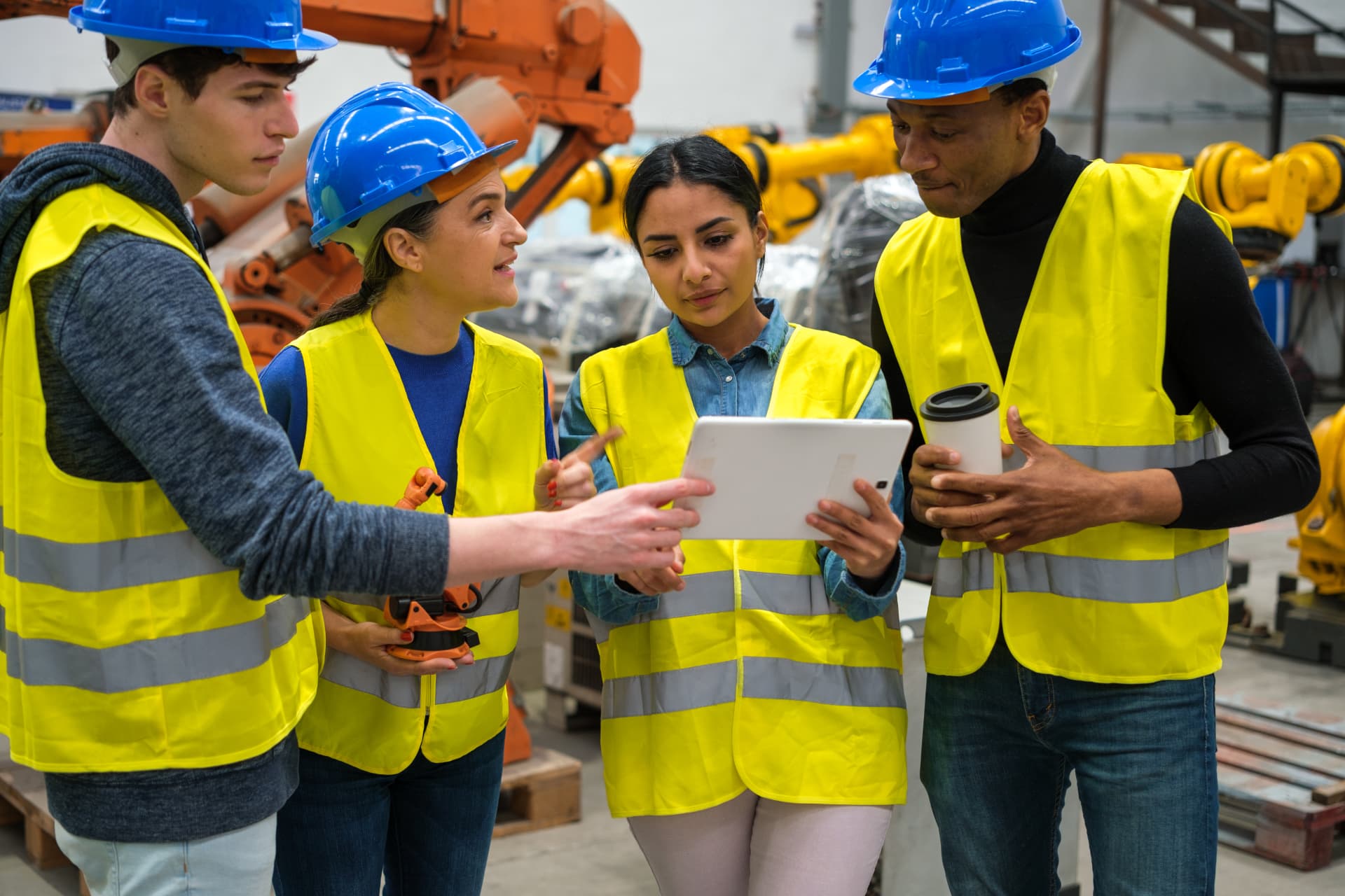 Manufacturing team in hard hats and safety vests reviewing a tablet on the plant floor